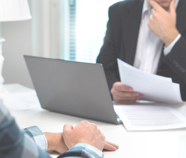Two men are sitting at a table with papers and a laptop