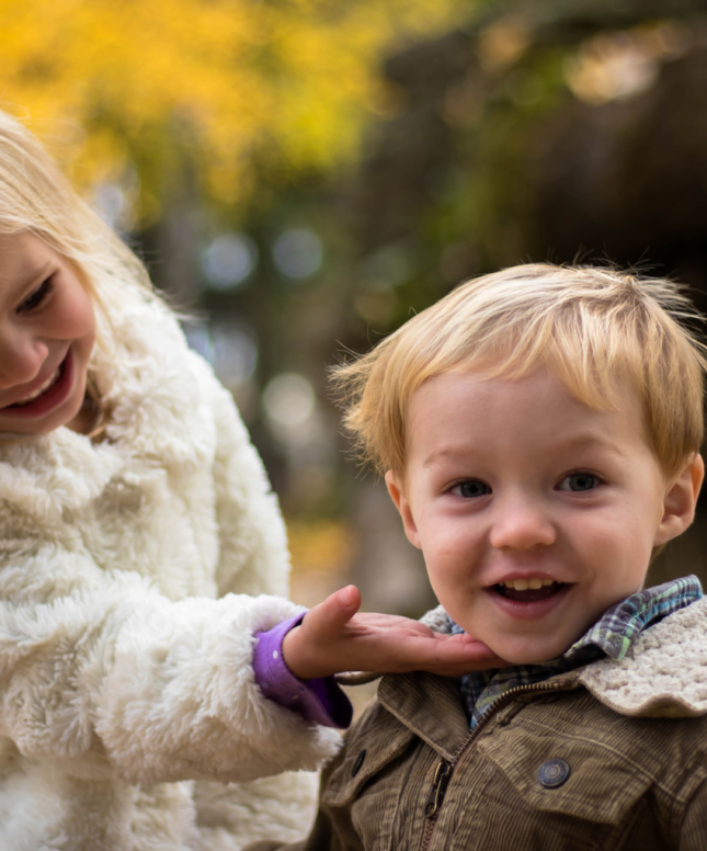 A young boy and girl. The girl is smiling at the boy and the boy is smiling at the camera