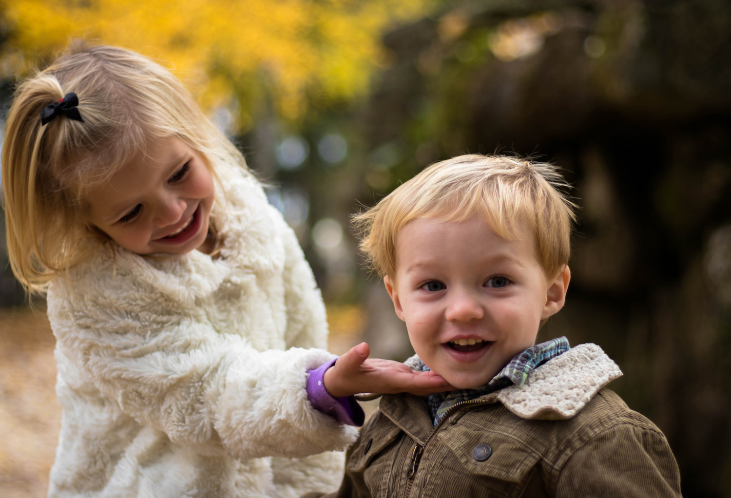 A young boy and girl. The girl is smiling at the boy and the boy is smiling at the camera