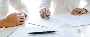 Two people are sitting at a table with papers and a pen looking over a will