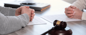 A man and a woman are sitting at a table with papers to file for divorce and a judge 's gavel
