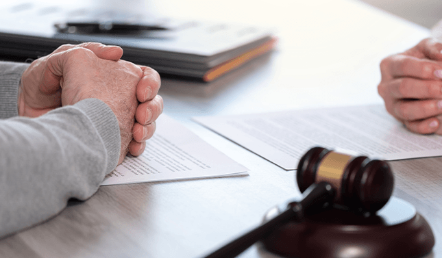 A man and a woman are sitting at a table with papers to file for divorce and a judge 's gavel